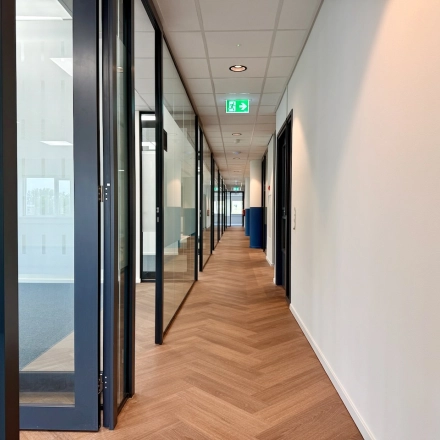 Een moderne kantoorgang met glazen deuren en houten vloer op Professor E.M. Meijerslaan in Amstelveen, geschikt voor kantoorruimte huren.