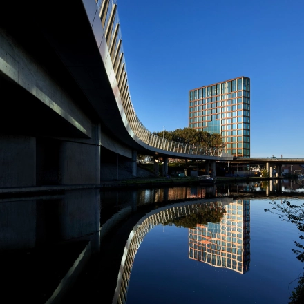 Moderne buitenkant van het kantoorpand aan H.J.E. Wenckebachweg 230-258, gelegen in Amsterdam Amstel Business Park, met reflecties in het water. Perfecte locatie voor kantoorruimte huren.