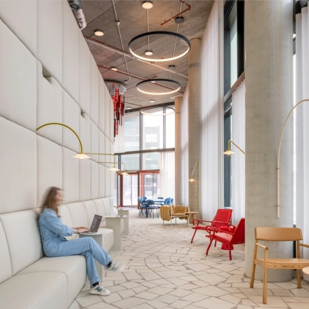 Lichte en moderne lounge in een kantoorpand aan H.J.E. Wenckebachweg 230-258, Amsterdam met gedempte verlichting en stijlvolle zitbanken. Een persoon werkt op een laptop, wat de zakelijke sfeer benadrukt.