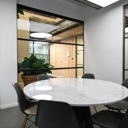 Kantoorruimte in Amsterdam Amstel Business Park met een ronde marmeren tafel en moderne zwarte stoelen, uitzicht op een plantenbak en glazen wanden. Ideaal voor huren als vergaderruimte.