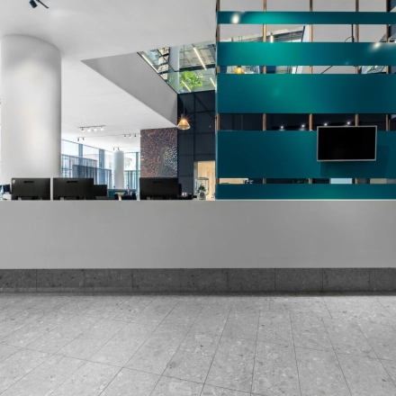 Moderne receptieruimte in kantoorpand Trompenburgstraat 2c, Amsterdam, met strakke balie en verlichte plafondpanelen. Ideaal voor bedrijven die naar kantoorruimte huren in Amstel Business Park zoeken.