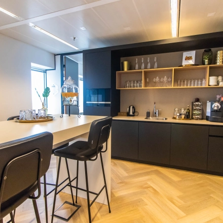 Moderne pantry in een kantoorpand op Amstelplein 8, Amsterdam Amstel, met hoge stoelen en een koffiezetapparaat. Ideaal voor kantoorruimte huren.