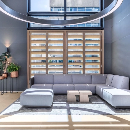 Moderne kantoorruimte huren aan Amstelplein 8 in Amsterdam Amstel met een strakke, lichte inrichting voorzien van comfortabele grijze banken en houten accenten, perfect voor zakelijke gesprekken of informele bijeenkomsten.