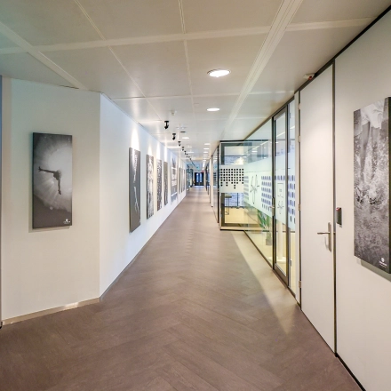 Kantoorruimte in Amsterdam Amstel met lange gang, kunstwerken aan de muur en zicht op glazen kantoorruimte voor verhuur.