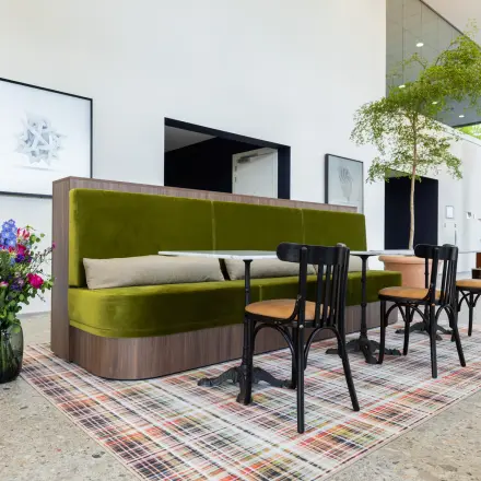 Modern gemeubileerde kantoorruimte in Amsterdam Amstel met groene bank, houten stoelen en een kleurrijk vloerkleed voor flexibel werken.