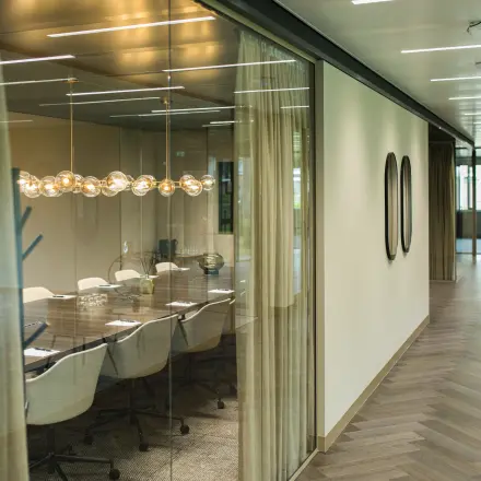 Moderne kantoorruimte in Amsterdam Buitenveldert met glazen wanden, stijlvolle verlichtingsarmaturen en een grote vergadertafel. Ideaal voor kantoorruimte huren.