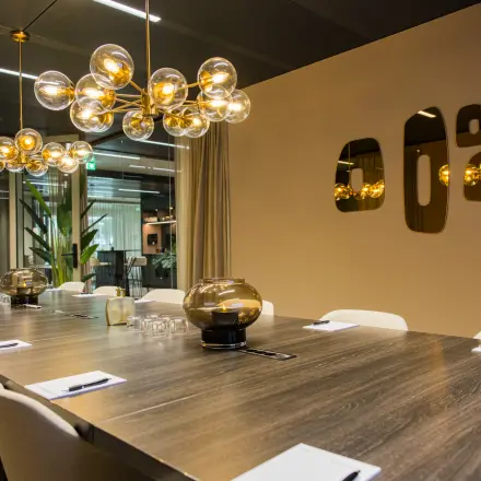 Stijlvolle vergaderruimte in Amsterdam Buitenveldert met lange houten tafel, moderne stoelen en opvallende verlichting, ideaal voor kantoorruimte huren.