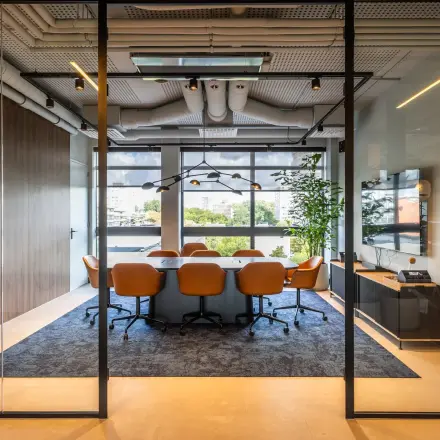 Vergaderruimte in kantoorpand met lange tafel, bruine leren stoelen en groot raam met uitzicht op Amsterdam Buitenveldert. Modern interieur met glazen wanden en houten accenten, geschikt voor kantoorruimte huren.