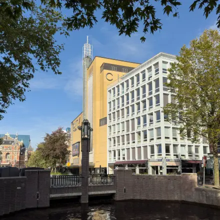Kantoorpand aan Kleine Gartmanplantsoen 21 in Amsterdam Centrum met moderne gevel en omringd door bomen en water.