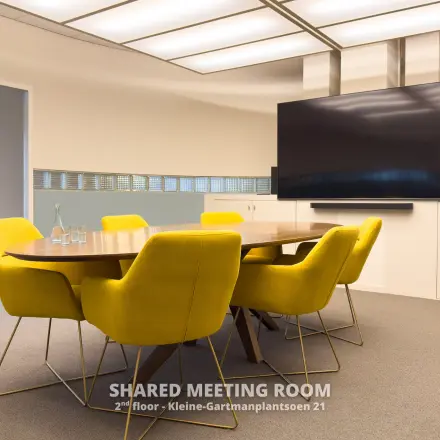 Vergaderruimte met felgele stoelen rond een houten tafel in het kantoorgebouw op Kleine Gartmanplantsoen 21, Amsterdam Centrum. Een televisie scherm aan de muur en een bloemstuk completeren de ruimte.
