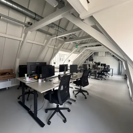 Moderne kantoorruimte te huur in Amsterdam Centrum, gelegen op Kloveniersburgwal 131K, ingericht met bureaus en computerschermen onder een karakteristiek schuin dak.