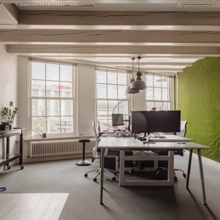 Modern kantoorpand in Amsterdam Centrum met bureaus en stoelen nabij een groene wand aan Prins Hendrikkade 14. Grote ramen zorgen voor veel lichtinval. Geschikt voor kantoorruimte huren.