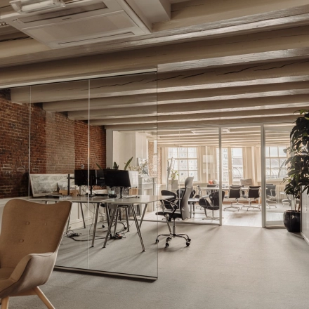 Kantoorruimte huren op Prins Hendrikkade 14 in Amsterdam Centrum met industriële bakstenen muren, glazen scheidingswanden en meerdere werkplekken met bureaus en stoelen.