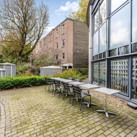 Buitenruimte van kantoorpand op Stadhouderskade 55 in Amsterdam Centrum met tafels en stoelen, omringd door groene beplanting en naastliggende gebouwen.