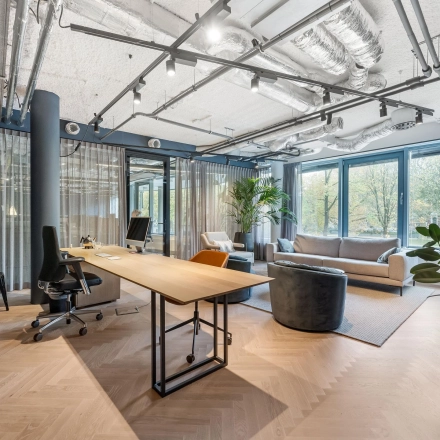 Modern ingerichte kantoorruimte aan Stadhouderskade 55 in Amsterdam Centrum, met grote ramen die uitzicht bieden op groen. Stijlvolle werkplekken met houten vloeren en comfortabele stoelen.