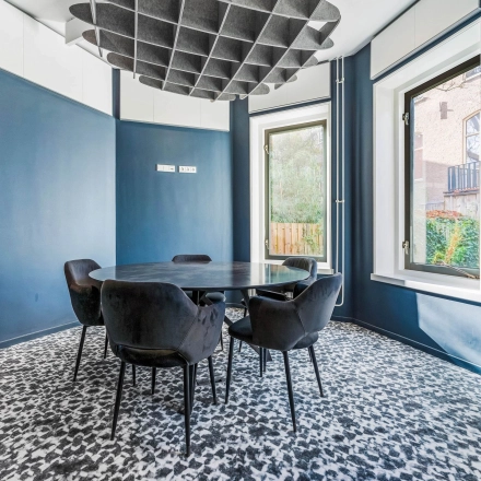 Een stijlvolle vergaderruimte met ronde tafel en vijf stoelen, gelegen in een kantoorpand aan de Stadhouderskade 55, Amsterdam Centrum. Grote ramen bieden veel natuurlijk licht.