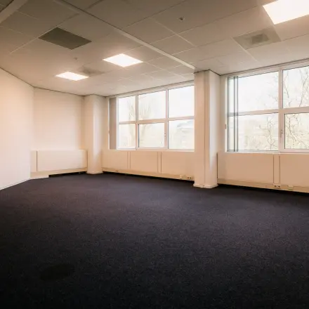 Ruime kantoorkamer op Overschiestraat 182, Amsterdam De Schinkel voor kantoorruimte huren. Grote ramen zorgen voor natuurlijk licht op de blauwe vloeren, ideaal voor een flexibel indeelbare werkruimte.