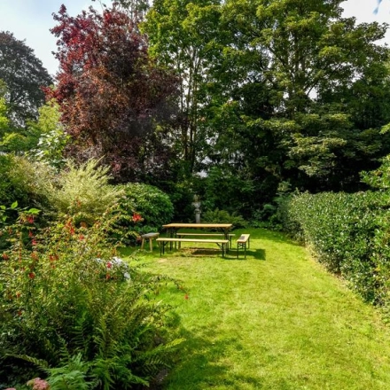 Groene buitenruimte van kantoor aan Herengracht 338, Amsterdam Grachtengordel, met grasveld en houten picknicktafel, omgeven door bloeiende struiken en bomen.