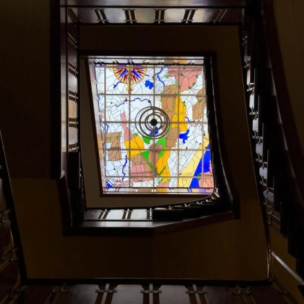 Een kleurrijk glas-in-loodraam met abstracte vormen, gevat in een donkere houten lijst, in een kantoorpand aan Herengracht 582-584, Amsterdam Grachtengordel.