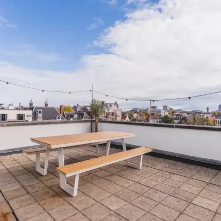 Dakterras in Amsterdam Grachtengordel met houten tafel en banken, uitzicht op de stad. Ideaal voor ontspanning tijdens kantooruren in dit kantoorpand aan de Herengracht 582-584.