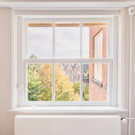 Een licht kantoorpand in de Amsterdamse Grachtengordel met witgeschilderde muren en een groot raam dat uitzicht biedt op de groene omgeving en karakteristieke gebouwen.