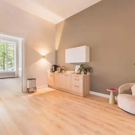 Een lichte en uitnodigende kantoorruimte met houten vloer, een kitchenette, en comfortabele zitgelegenheid aan de Herengracht in Amsterdam, ideaal om te huren als kantoorpand.