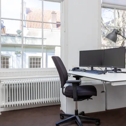 Lichte kantoorruimte met bureau, stoel en twee computerschermen, gelegen aan de Keizersgracht 62-64 in de Amsterdam Grachtengordel.