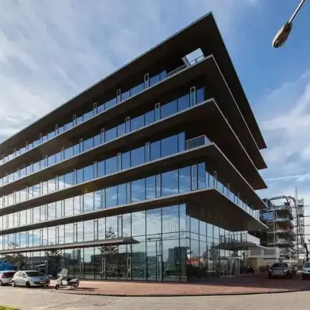 Modern kantoorpand op de Moermanskkade 303 in Amsterdam Houthavens, ideaal voor kantoorruimte huren. Het glazen gebouw weerspiegelt de lucht, met enkele auto's voor het pand geparkeerd.