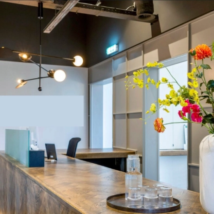 Moderne receptie in het kantoorpand op Meeuwenlaan 98-100 in Amsterdam Noord, met een stijlvolle balie en kleurrijke bloemen. Perfect voor wie kantoorruimte wil huren in een inspirerende omgeving.
