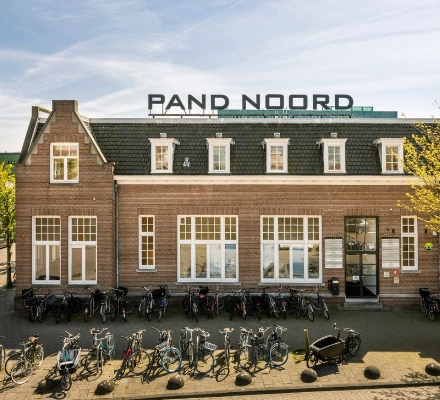 Kantoorgebouw aan de Meeuwenlaan 98-100 in Amsterdam Noord met een bakstenen gevel en fietsenrekken voor de deur. Ideaal voor wie kantoorruimte wil huren in een levendige omgeving.