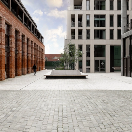 Buitenaanzicht van een modern kantoorpand op Papaverhof 58 in Amsterdam Noord, met elegante bakstenen en glasconstructie. Een enkele persoon loopt over het plein voor het gebouw.