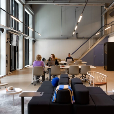 Kantoorruimte huren aan Papaverhof 58, Amsterdam Noord met moderne werkplekken en grote ramen. Verschillende mensen zijn bezig met zakelijke activiteiten aan tafels.
