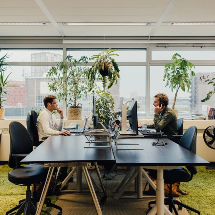 Kantoorruimte huren op TT Vasumweg 44 in Amsterdam Noord met uitzicht en veel groen. Twee mensen voeren zakelijke activiteiten uit aan hun bureaus.