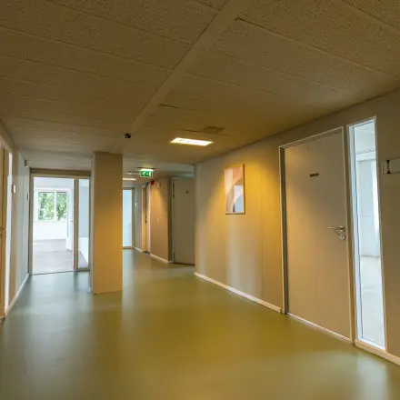 Een moderne gang in een kantoorpand op James Wattstraat 71, Amsterdam Oost, met goed verlichte open deuren die naar verschillende kantoren leiden.