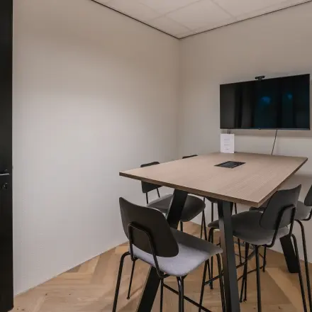 Moderne vergaderruimte in een kantoorpand op John M. Keynesplein 4-10, Amsterdam Riekerpolder, voorzien van een tafel met zes stoelen en een scherm aan de wand voor presentaties.