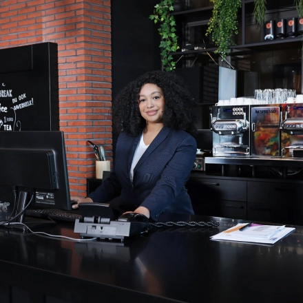 Zakelijke vrouw werkt achter de balie in een stijlvol kantoorpand op Teleportboulevard 110 in Amsterdam Sloterdijk. Op de achtergrond zijn koffiemachines en groene planten zichtbaar.