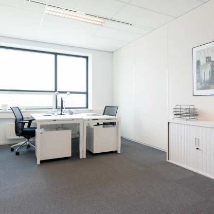 Goed verlichte kantoorruimte huren aan Teleportboulevard 110 in Amsterdam Sloterdijk met strak interieur, twee bureaus en een grote raam. Ideaal voor een productieve werksfeer in een kantoorpand.
