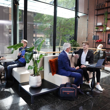 Moderne kantoorruimte aan de Teleportboulevard 110 in Amsterdam Sloterdijk met mensen die vergaderen en koffie drinken tussen planten en stijlvol meubilair.