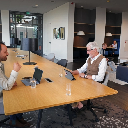 Zakelijke mensen werken in een moderne kantoorruimte met lange houten tafel en comfortabele stoelen in Amsterdam Sloterdijk aan de Teleportboulevard 110.