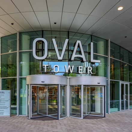 Ingang van een modern kantoorpand aan De Entree 99-197 in Amsterdam Zuid-Oost, met glazen deuren en groot OVAL TOWER bord.