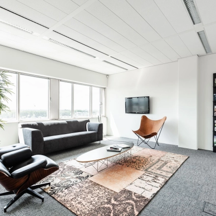 Lichte kantoorruimte met zitgedeelte inclusief sofa, fauteuils en een tapijt, ideaal om te huren op Herikerbergweg 240-286 in Amsterdam Zuid-Oost.