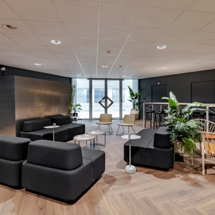 Moderne, smaakvolle lounge in een kantoorpand op Hoogoorddreef 60, Amsterdam Zuid-Oost. Ruime zitgelegenheid met stijlvolle meubels en groene planten, perfect om te netwerken of te ontspannen tijdens het huren van kantoorruimte.