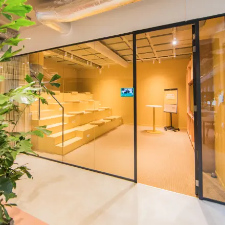 Moderne kantoorlounge met glazen wand, industrieel plafond en zitgedeelte, ideaal voor kantoorruimte huren in Amsterdam Zuid-Oost.