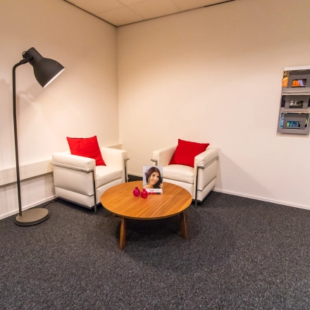 Kantoorruimte te huur aan de Hullenbergweg 278 in Amsterdam Zuid-Oost, met twee witte fauteuils, rode kussens en een houten salontafel.