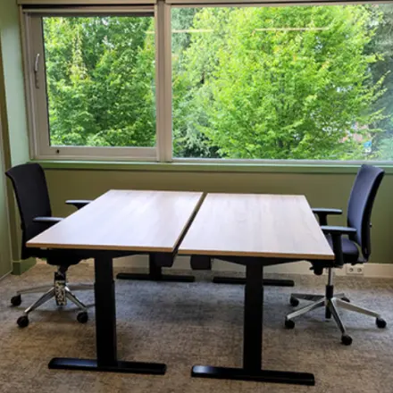 Kantoorruimte huren op Johan Cruijff Boulevard 89 in Amsterdam Zuid-Oost met twee bureaus en stoelen voor een groene muur met grote ramen.