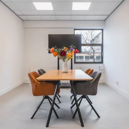 Vergaderruimte in kantoorpand aan Paasheuvelweg 20, Amsterdam Zuid-Oost, met houten tafel en kleurrijke bloemen. Kantoorruimte huren in een moderne setting.