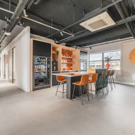 Moderne kantoorruimte op Paasheuvelweg 20, Amsterdam Zuid-Oost met een gemeubileerd interieur, voorzien van hoge tafels en een verkoopautomaat voor snacks en drankjes, ideaal voor wie een kantoorruimte wil huren.