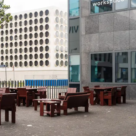 Exterieur van een kantoorpand aan de Barbara Strozzilaan 101, Amsterdam Zuidas, met houten zitplaatsen buiten. Ideaal voor wie kantoorruimte huren wil in een dynamisch omgeving.