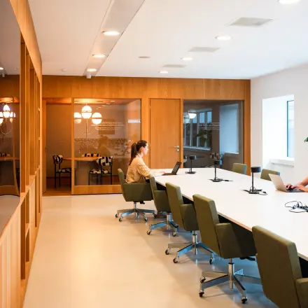 Stijlvolle vergaderruimte op Barbara Strozzilaan 101, Amsterdam Zuidas, met lange tafel voor zakelijke ontmoetingen. Twee personen voeren zakelijke activiteiten uit op laptops.