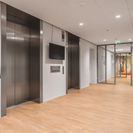 Moderne ontvangsthal op Claude Debussylaan 10 in Amsterdam Zuidas, met twee liften en een tv aan de muur. Perfecte locatie voor kantoorruimte huren met toegang tot diverse kantoren.
